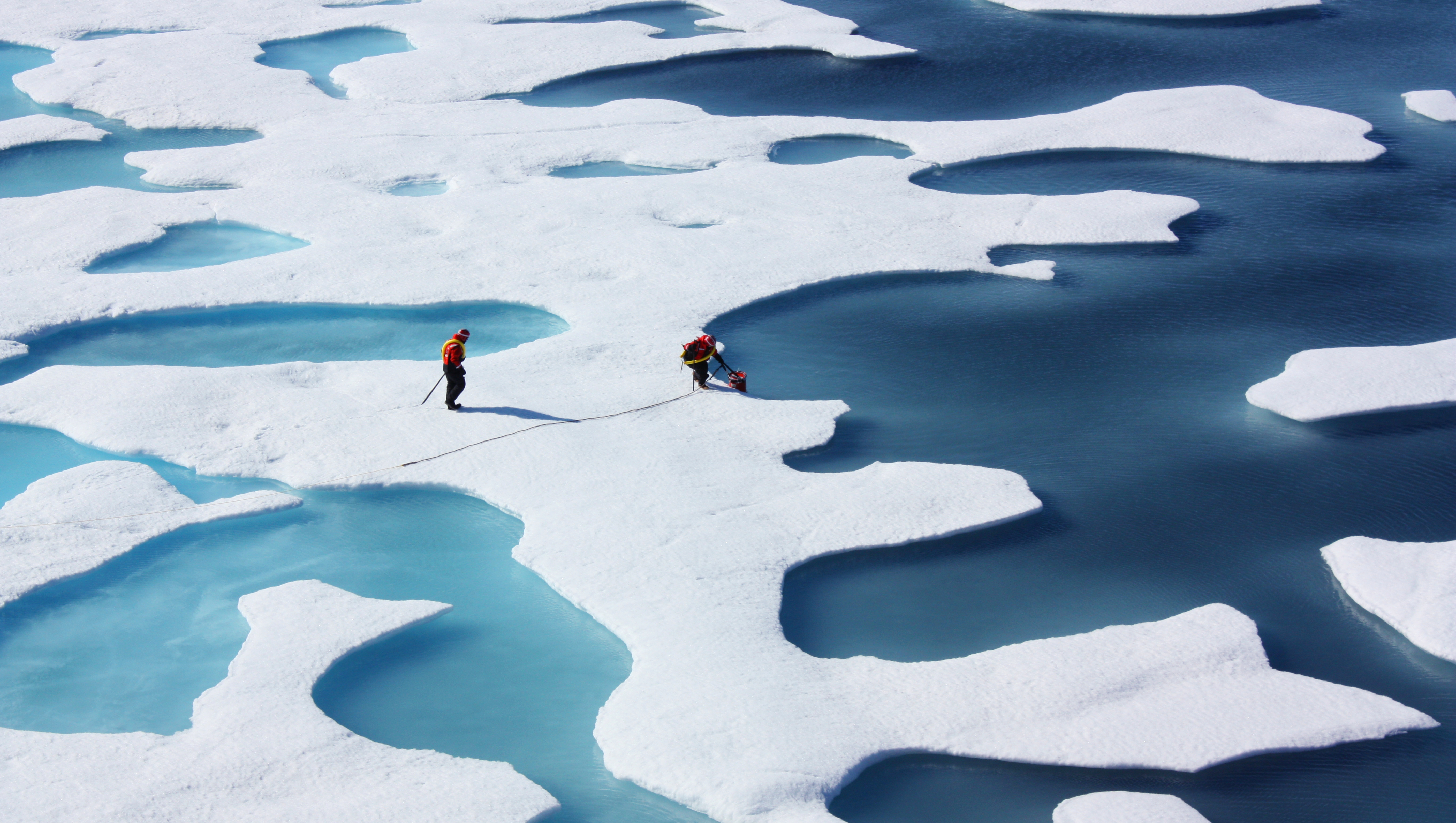 ICESCAPE任务的两名研究人员站在冰山上，将桶浸入水中.