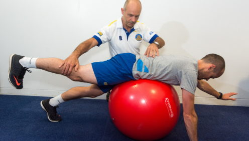 A TeamBath physiotherapist treating a man, who is lying facedown on an exercise ball
