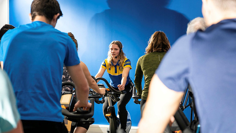A fitness instructor leads a group on exercise bikes