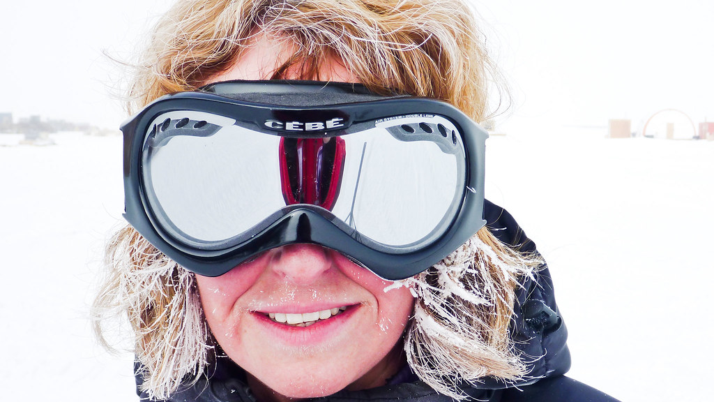 A researcher in snow protection clothes smiles into the camera against a polar background.