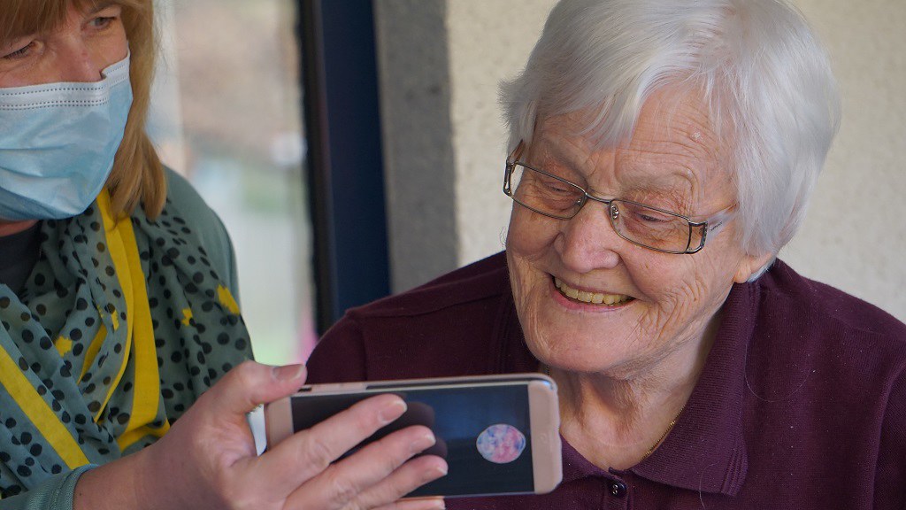一名医疗专业人员正在帮助一位使用智能手机的老年妇女