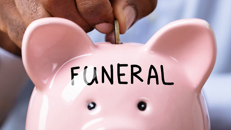 Coin being added to piggy bank labelled 'Funeral' 