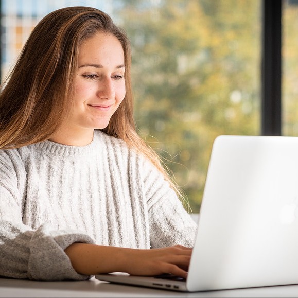 Female student with long blond hair sat in front of her silver laptop working