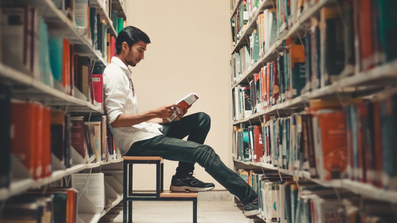 一个学生在图书馆里，在两个书架之间读书