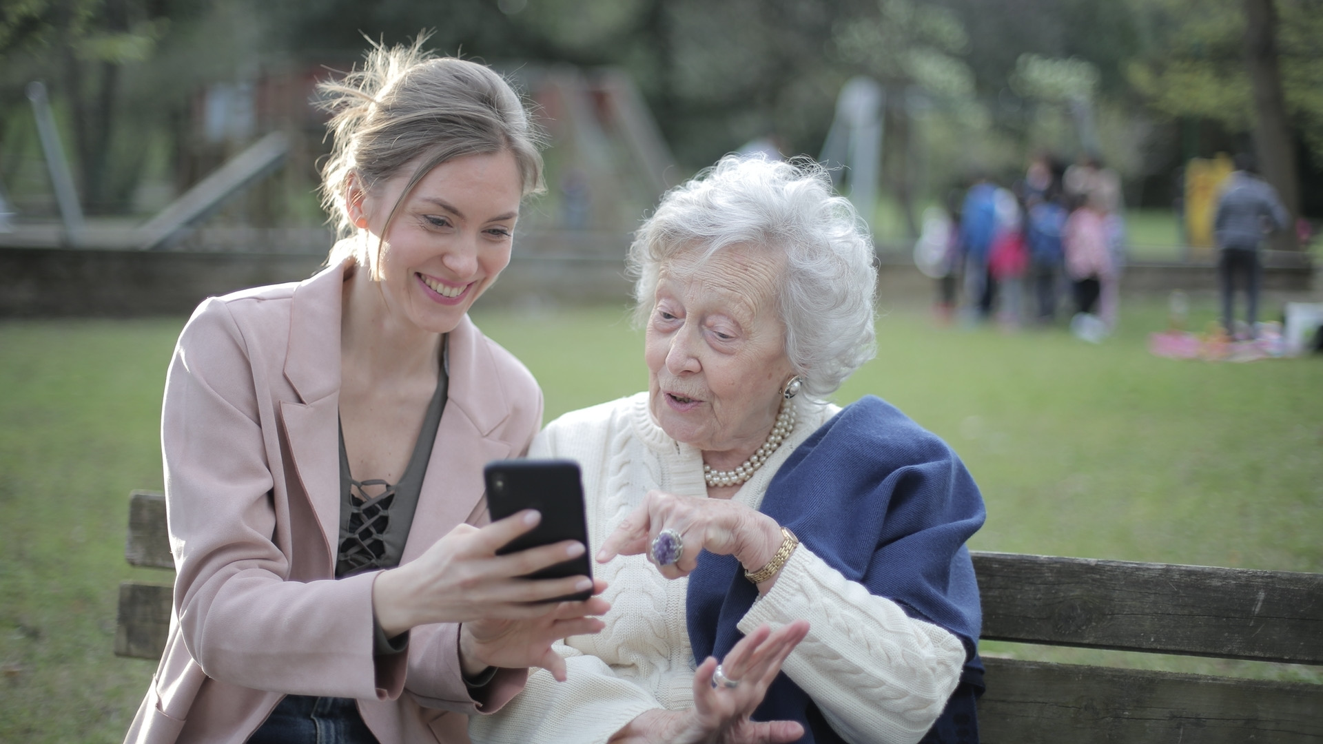 公园背景，一个年轻女性拿着手机给一位年长的女性看 
