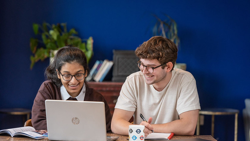 Two prospective students in a domestic setting smile as they look at a shared laptop.