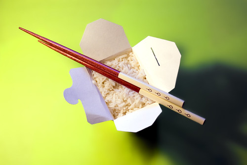 Overhead on rice and chop sticks in takeout box on green surface