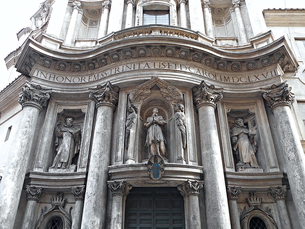 Front of San Carlo alle Quattro Fontane Church in Rome, which is a big light stone structure with three statues in the center and 4 columns along the front. 