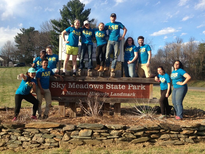 A group of college students in blue t-shirts that say "ASB," posing around a large sign that reads "Sky Meadows State Park A National Historic Landmark"