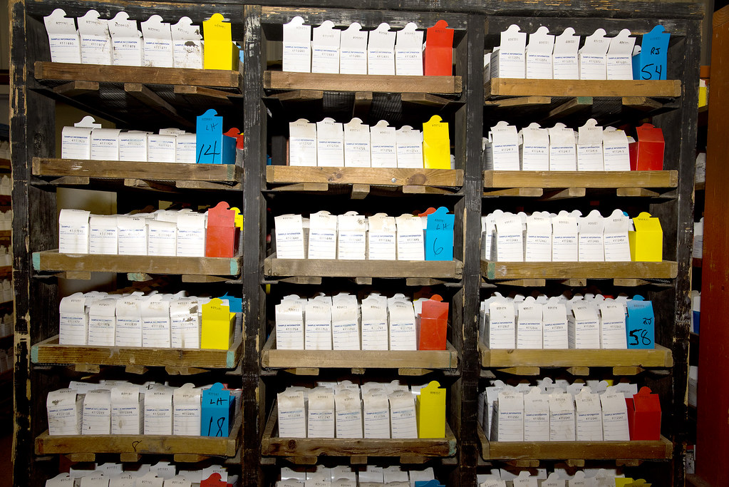 Shelves filled with hundreds of boxed soil samples stored at the Marianna Soil Test and Research Laboratory. The labeled sample boxes are organized in wooden racks, with color-coded dividers used to separate and identify groups of agricultural soil submissions for testing and recordkeeping.