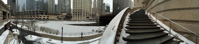 Panoramic of frozen Chicago River and snow capped staircase of Michigan Avenue bridge