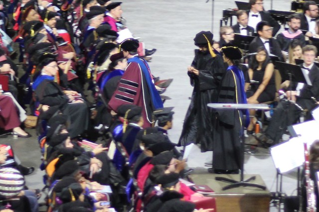 Simi walking off stage with her newly hooded PhD students, Nariman and Carl