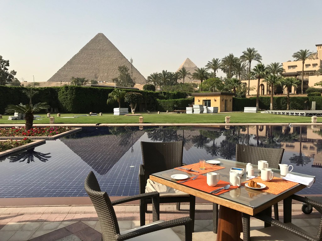 A table for two at the Marriott Mena House is set up outside on the courtyard next to a shallow pool. The view overlooks the Pyramids of Giza in the background.