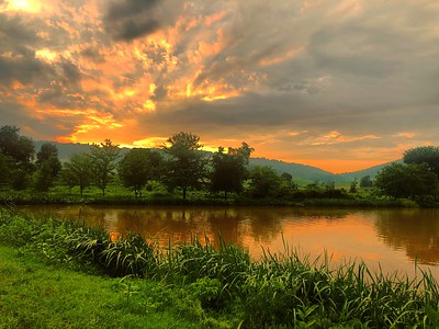 Orange and yellow rays bounce off of clouds during a sunset over Truner Pond
