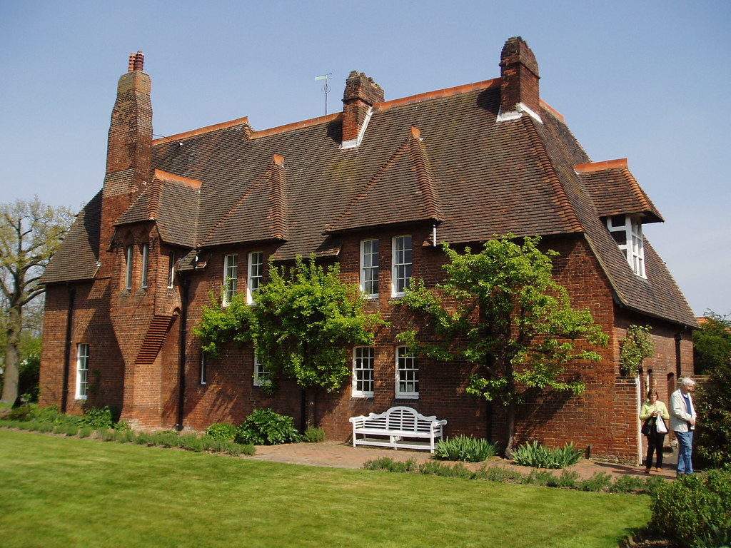 Red House: A photo of the deep brown estate with two trees along the front and mid-sized white panel windows. 
