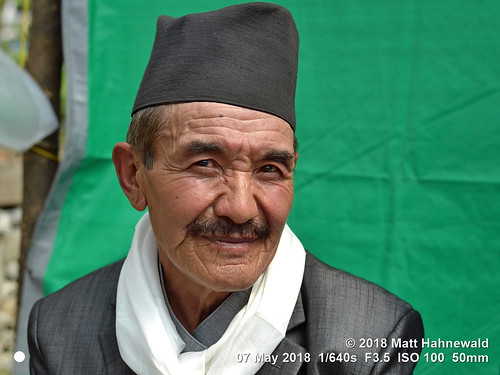 matthahnewaldphotography facingtheworld character head face eyes catchlights expression moustache cap hat shawl bhaadgaauletopi blackcap respect dignity travel socialevent ethnic local traditional cultural wedding celebration village tarkeghyang helambu himalayas nepal asia asian nepali sherpa hyolmo male elderly man backdrop nikond3100 primelens nikkorafs50mmf18g 50mm street portrait closeup threequarterview outdoor posingcamera wellgroomed manly serious trekking hiking clarity wrinkles colour person conceptual consensual lookingatcamera headshot