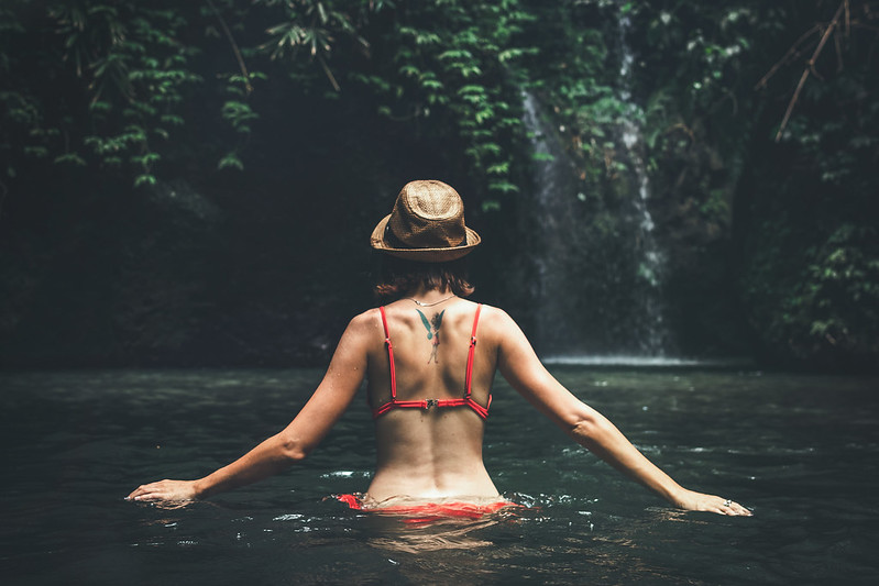 Young woman tourist with straw hat in the deep jungle with waterfall. Real adventure concept. Bali island.