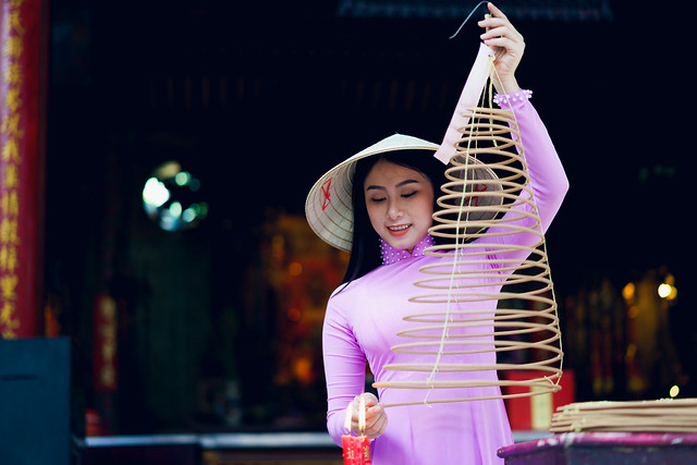Vietnamese woman in traditional dress praying with incense stick in the burning pot of the Chinese temple