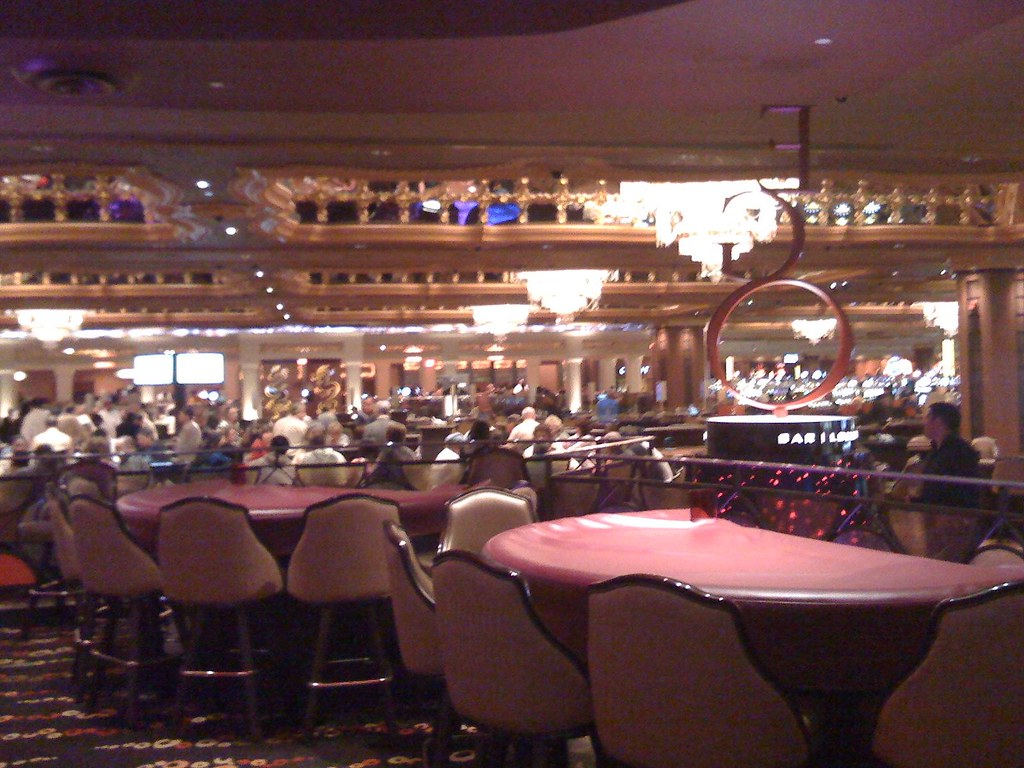 a large group of people sitting at a table with a bar - Casino floor
