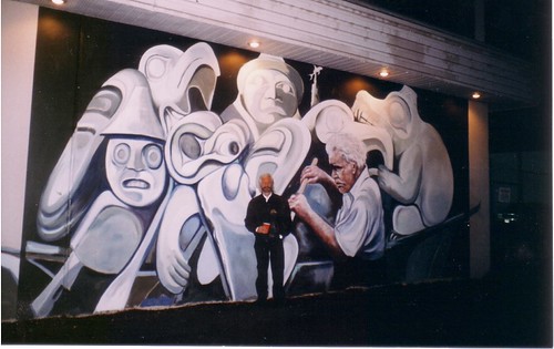 People standing before a black and white mural of mask faces