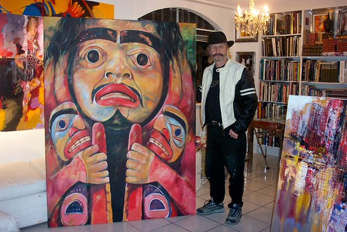 Artist standing beside a tall painting of a mask figure