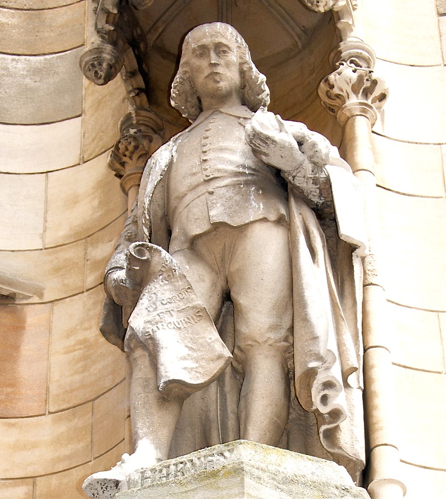 Sir Isaac Newton light-stone statue. He holds a scroll in his right hand and stands in a sassy-pose. 
