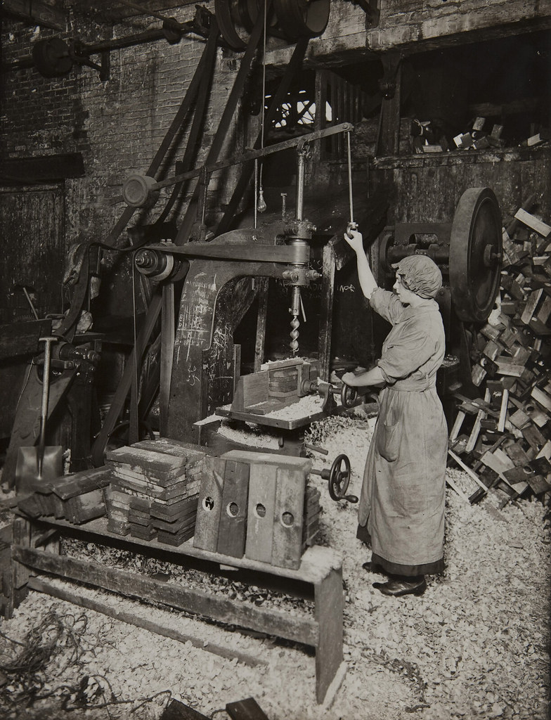 Woman operating boring machine; boring wooden reels for winding barbed wire