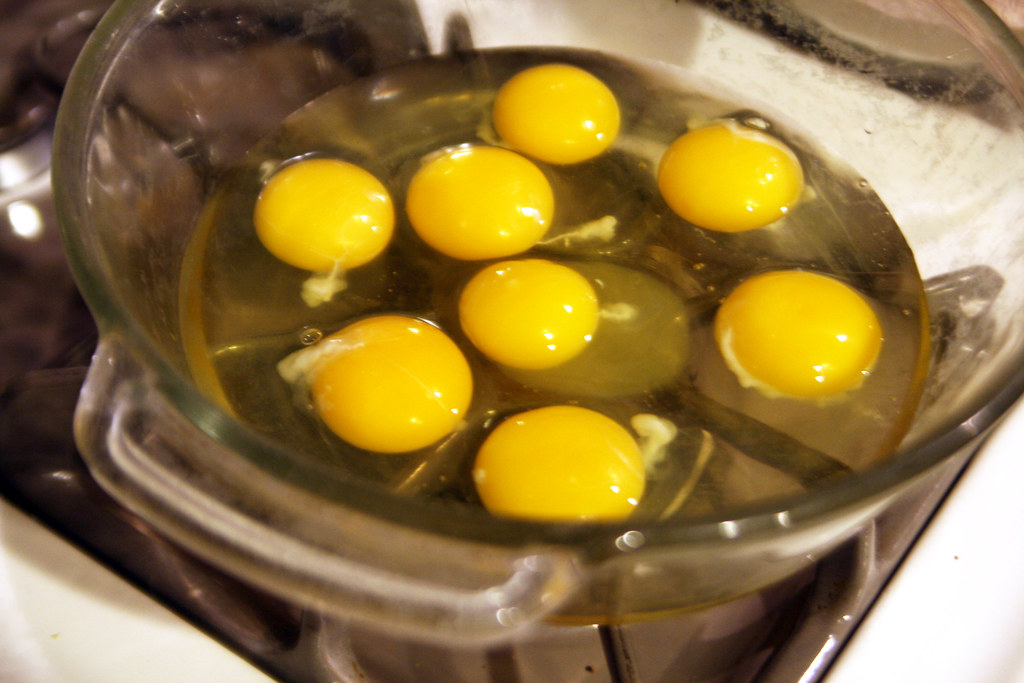 Multiple raw eggs cracked into a glass bowl for baking
