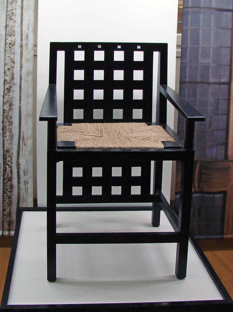 Siège de C.R. Mackintosh (The Lighthouse, Glasgow): Photo of a black chair with squares cut out of the back and a brown weaved seat. 