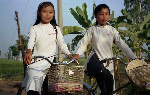2 girls in ao dais on bicycles; Mekong River Delta, Vietnam