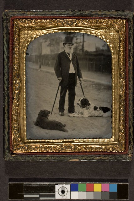 Unidentified standing man in top hat, with two dogs in outdoor setting