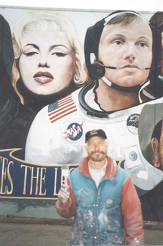 Artist standing beneath large portraits on a wall