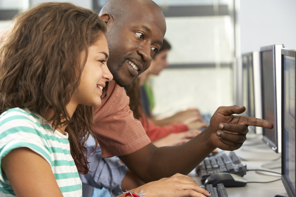 Black teacher helping a student at a computer