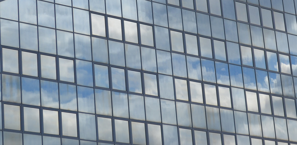 A flat grid of curtain wall glass filling the frame, each panel reflecting broken cloud and blue sky.