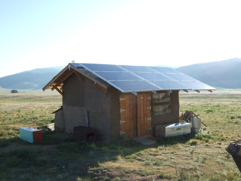 A shed in a grassland equipped with a large array of solar panels