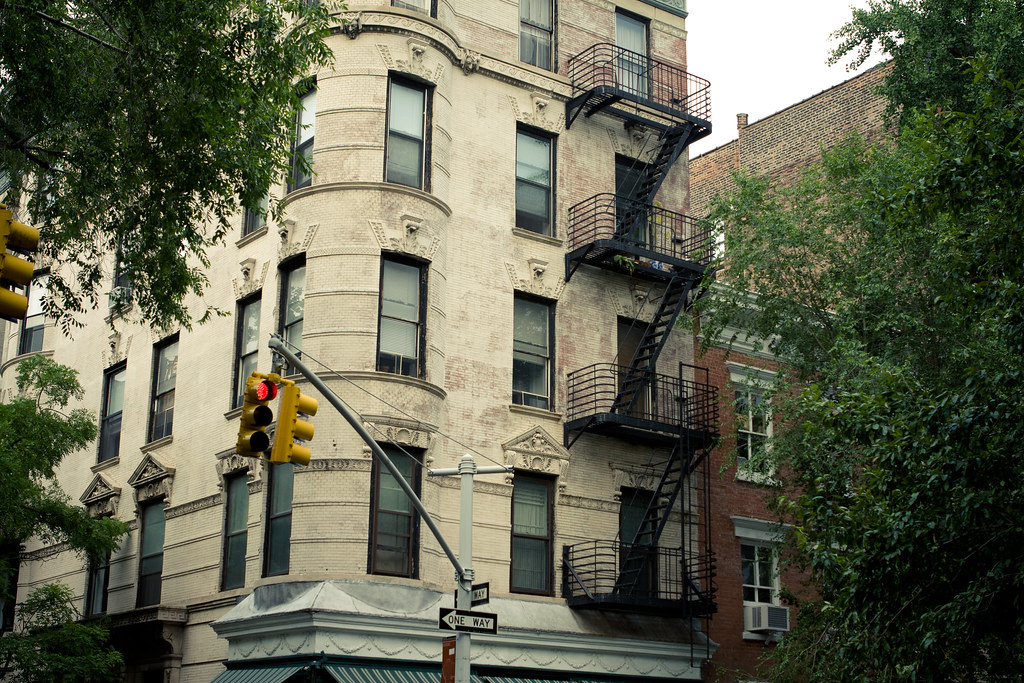 NYC brick apartment building with curved corner bay, fire escapes, traffic lights, and a One Way sign.