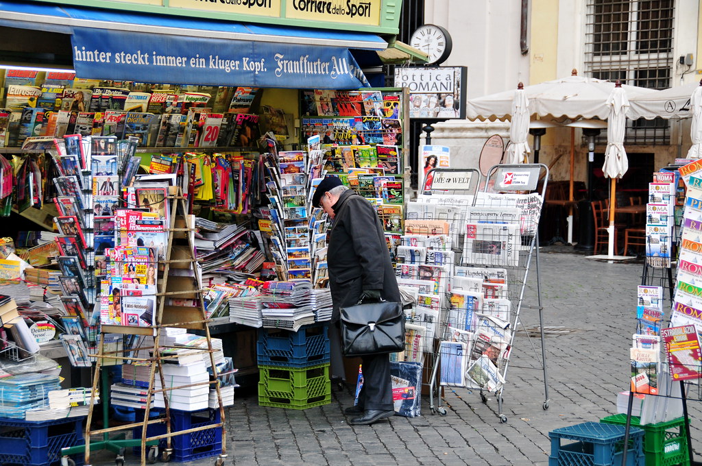 Photo of a city newsstand, with an individual browsing the newspapers and magazines