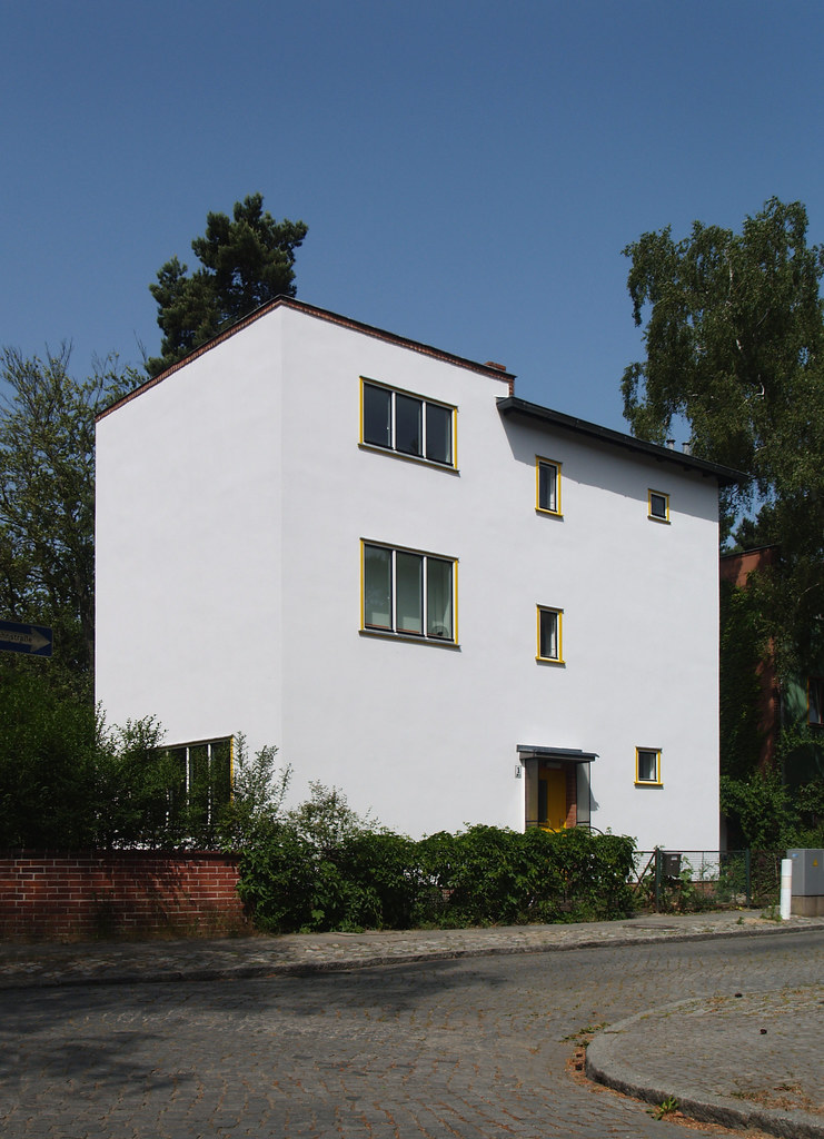 Waldsiedlung onkel toms hütte (1926-1932) - Bruno Taut: A simple white house with odd placed windows and a black roof. Moreover, there are bushes along the front. 