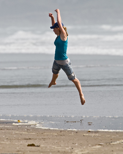 3 of 8 Girl dances (jumps) at water's edge on Morro Strand State Beach