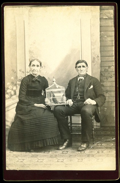 Man and woman seated in studio with blackbird in cage