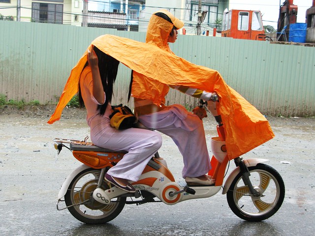 Moto girls in ao dai and an orange poncho - Mekong Delta, Vietnam