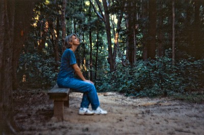 A women sits on a bench alone in the woods, listening to the world around her.