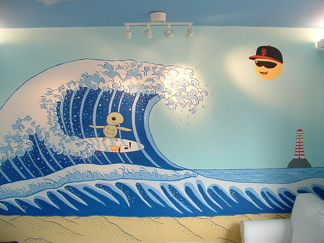 A photograph of a mural depicting a cute cartoon turtle riding a surfboard on a big wave