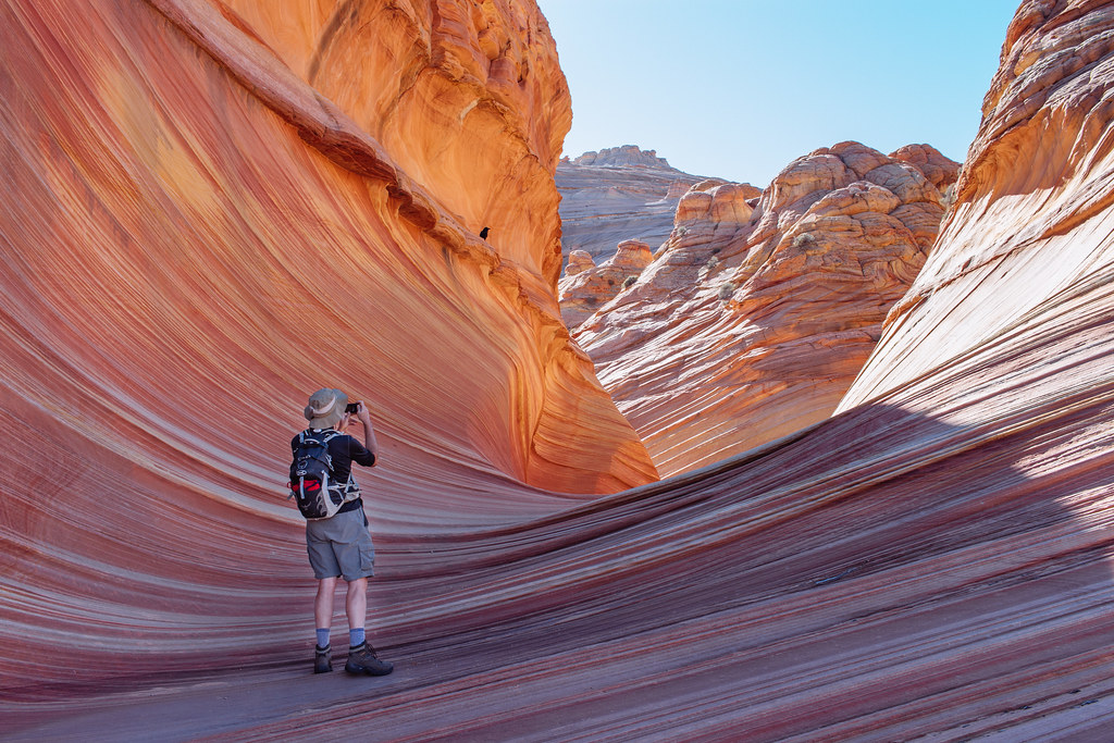 A hiker stands in a bowl of orange and white striped rock layers to take a picture