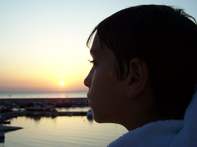 Kleiner Junge schaut sich einen Sonnenuntergang am Wasser an