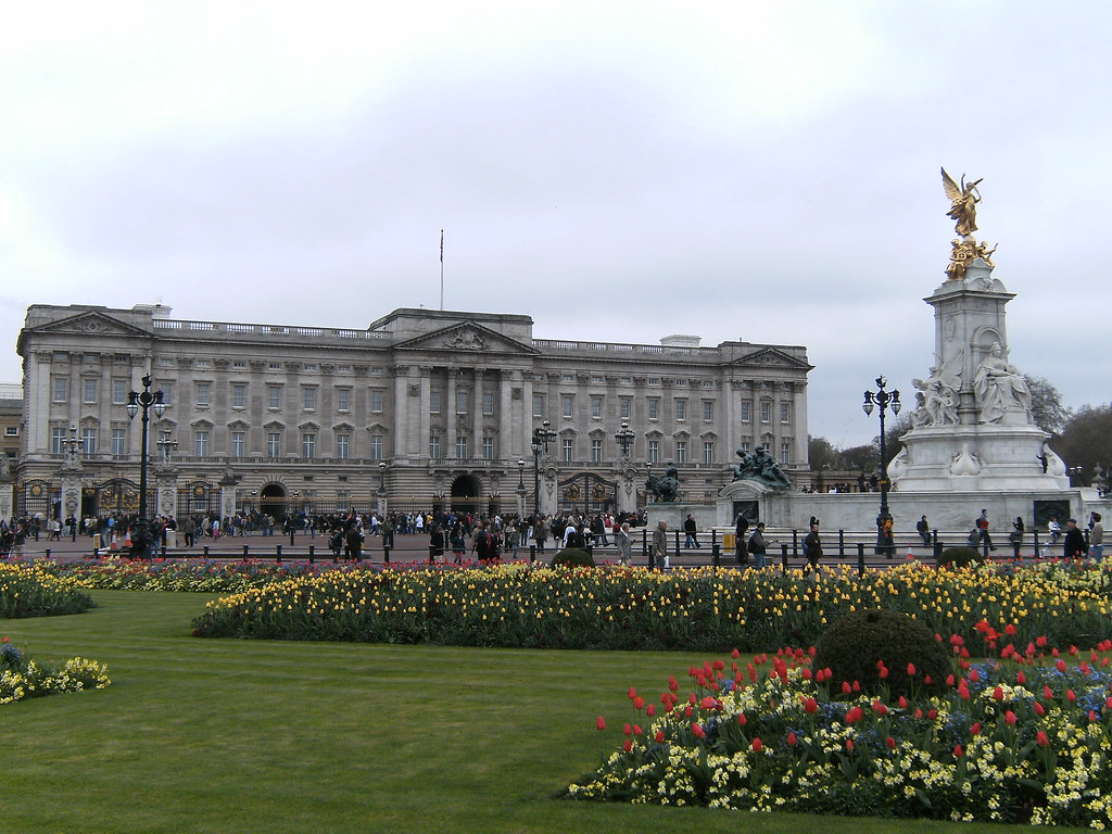 Buckingham Palace & Queen Victoria Memorial: The palace sits in the background, while a large garden with red and yellow flowers sit in the foreground. 