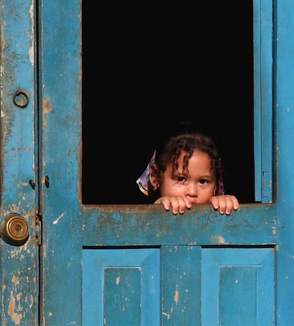 Young Cuban girl looking out her front door