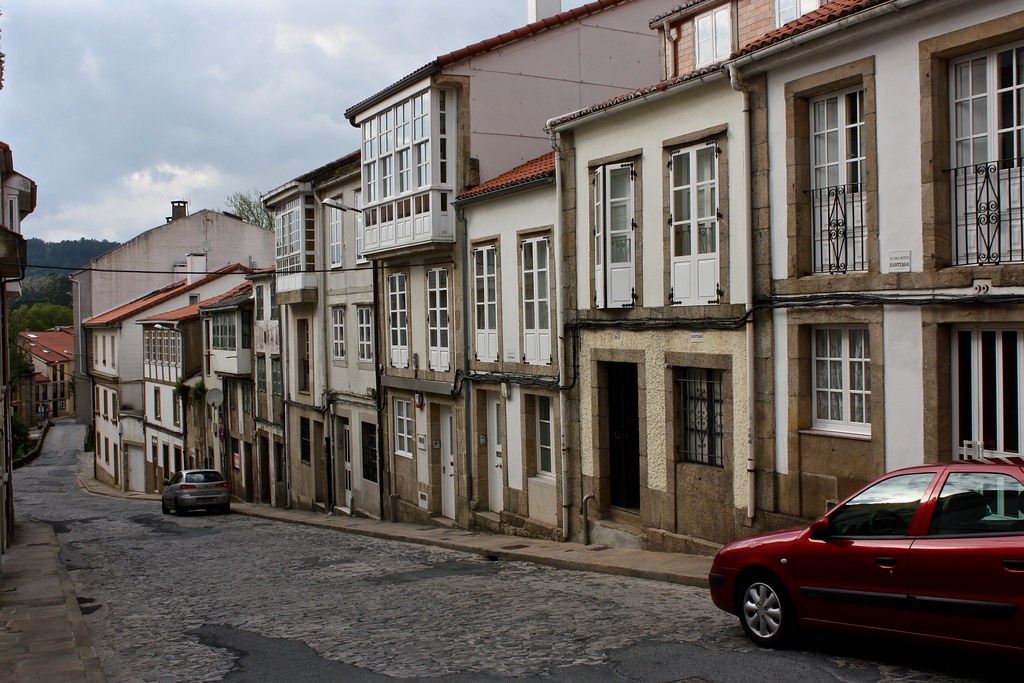 Granite stone houses with whitewashed walls and glassed in balconies are lined up along a cobblestone street