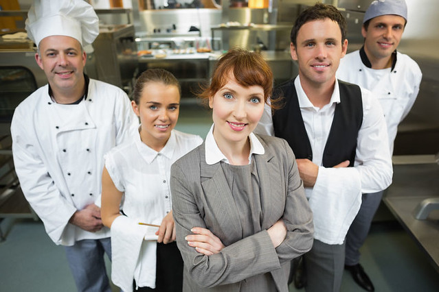Nice female manager posing with the staff in a modern kitchen catering