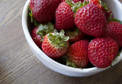Fresh strawberries in a white bowl on wooden surface